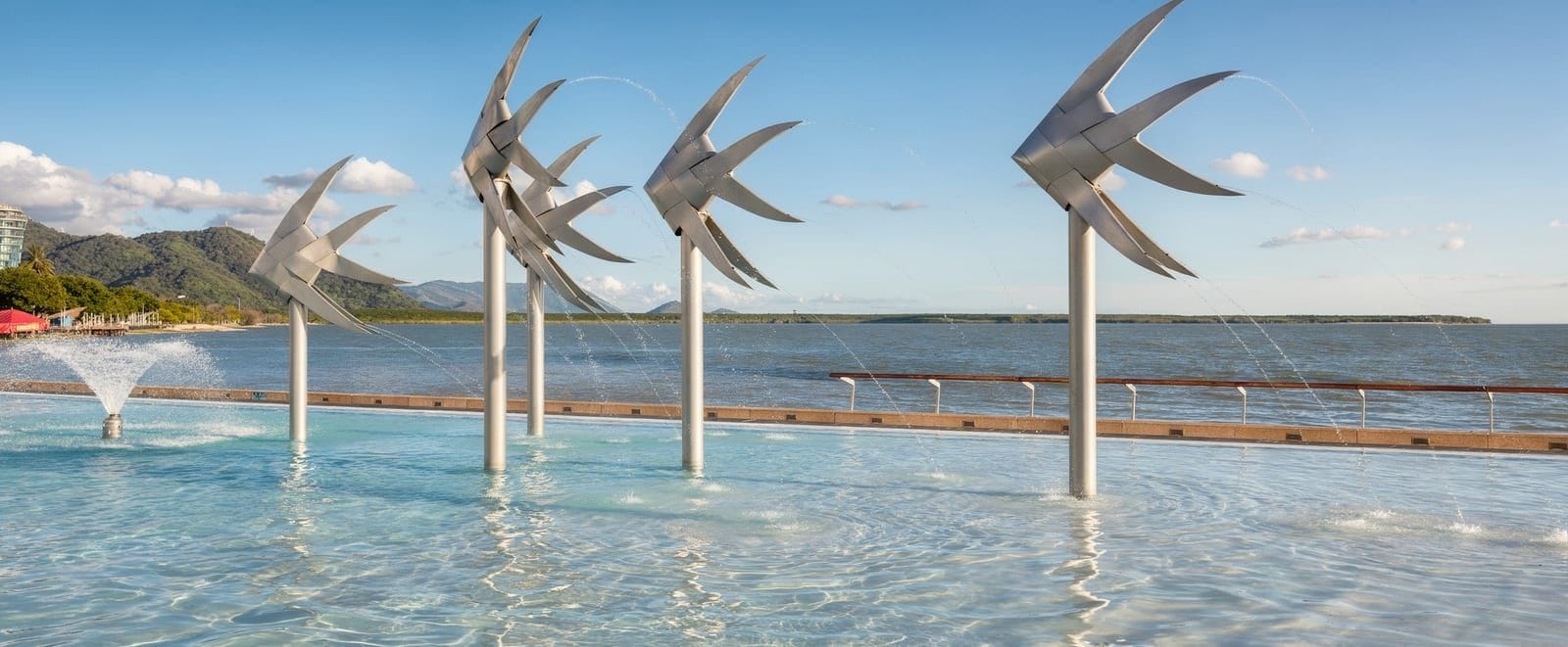 The turquoise Esplanade Lagoon in Cairns with its stainless-steel fish sculptures, looking out over the Coral Sea on a clear morning.